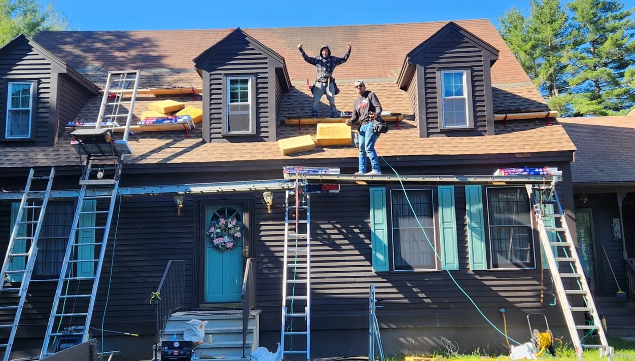 Two roofers installing shingles on a gambrel roof on a sunny day